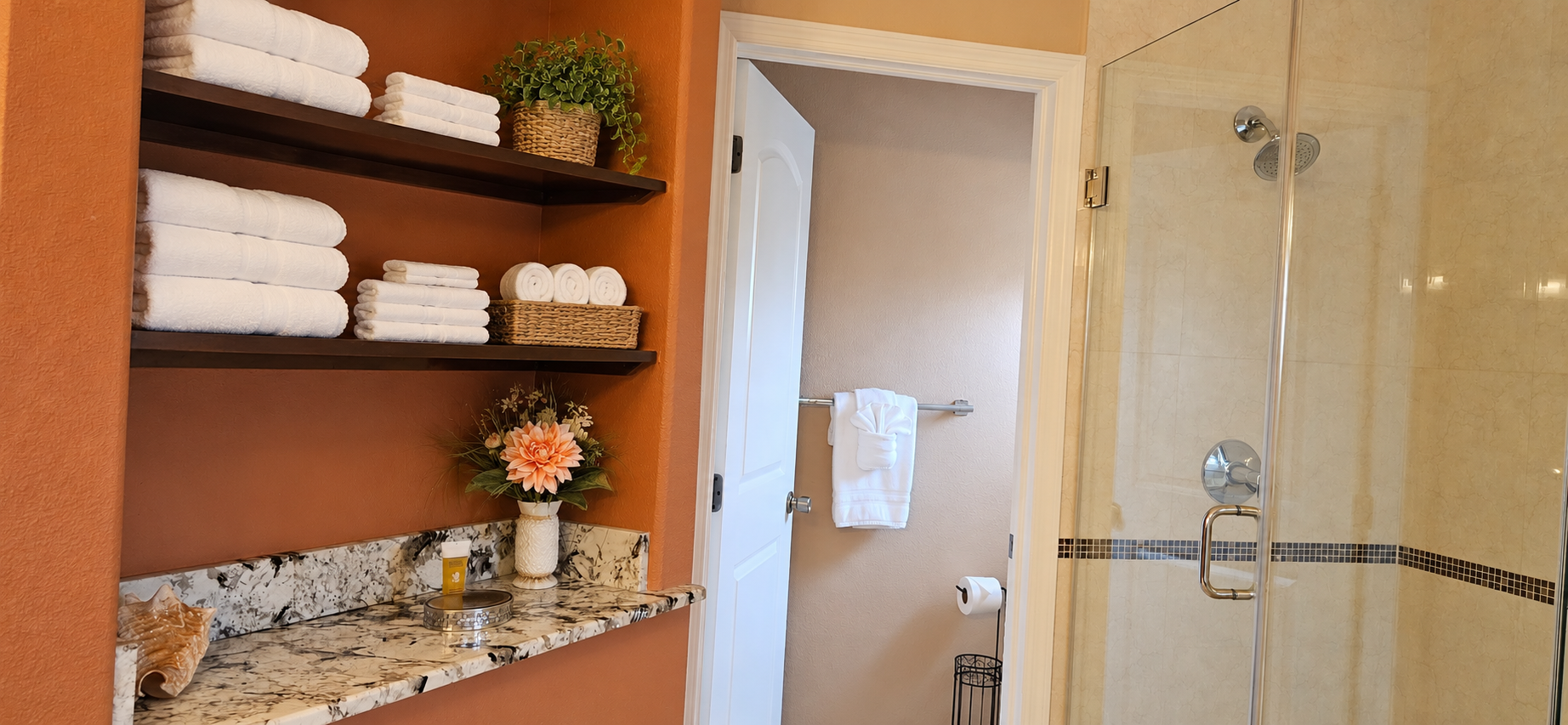 Master bathroom: built-in vanity shelving with plush bath towels and walk-in glass shower entrance