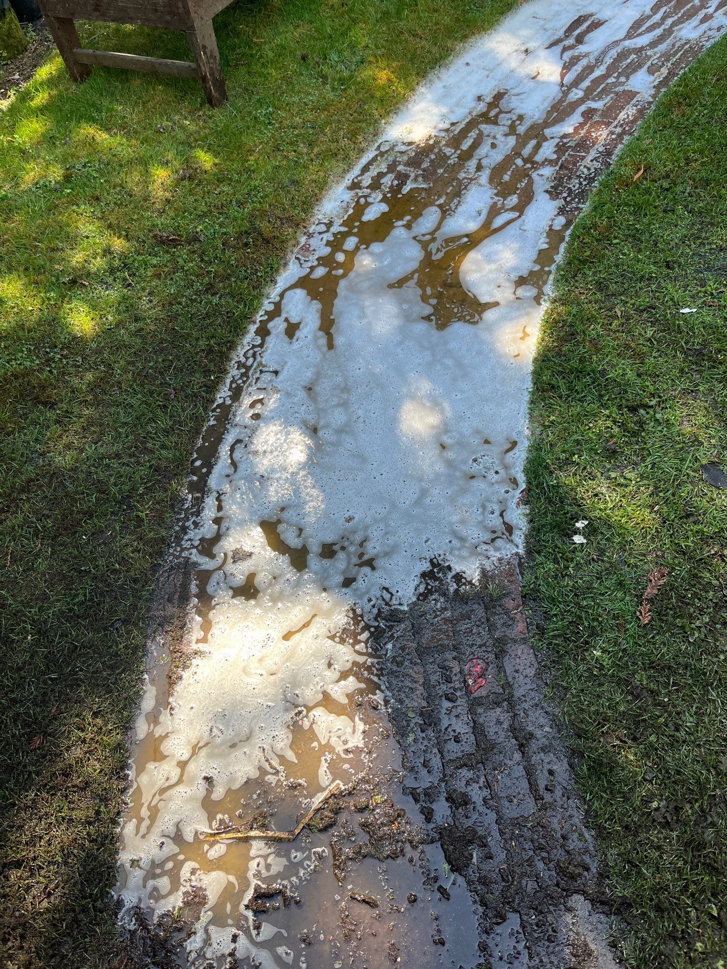 In-progress pressure washing — deep detergent foam lifting decades of compacted mud and algae from brick joints
