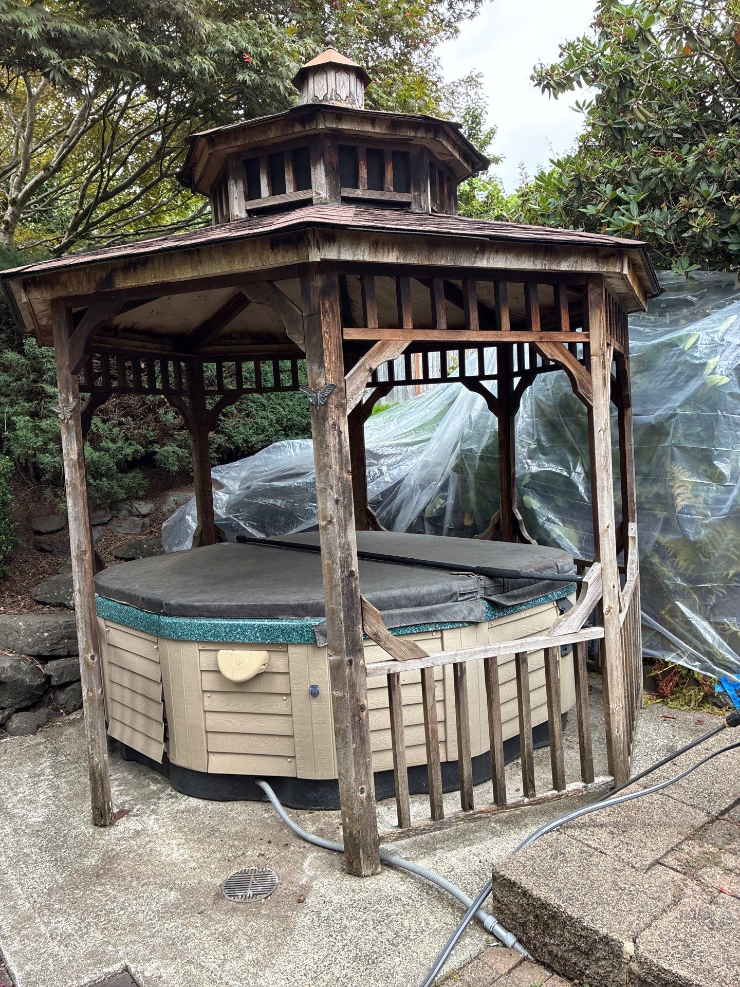 Before gazebo restoration — grayed weathered cedar timber and organic growth around spa