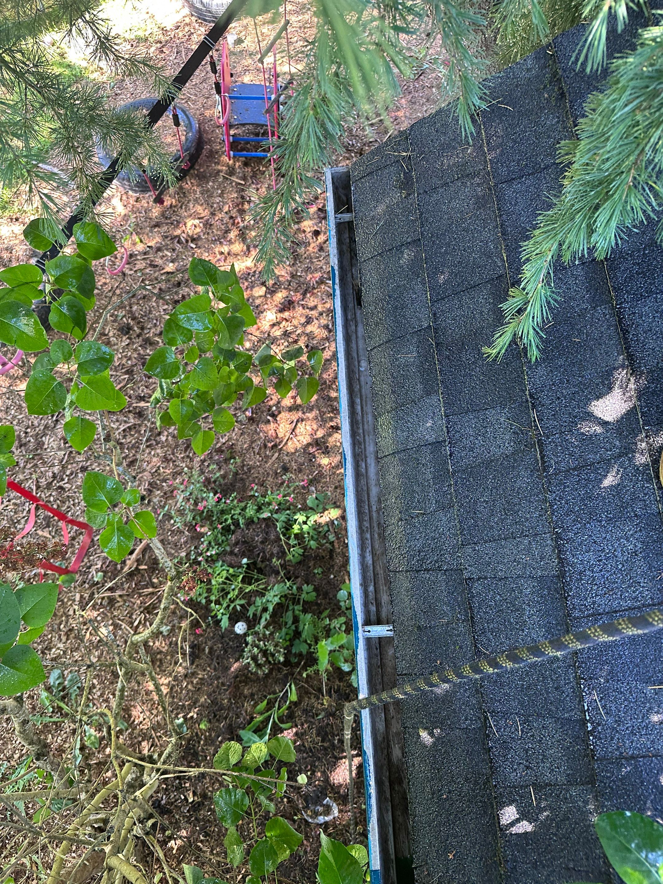In progress gutter cleaning — technician methodically scooping compacted debris from roof edge with safety rigging
