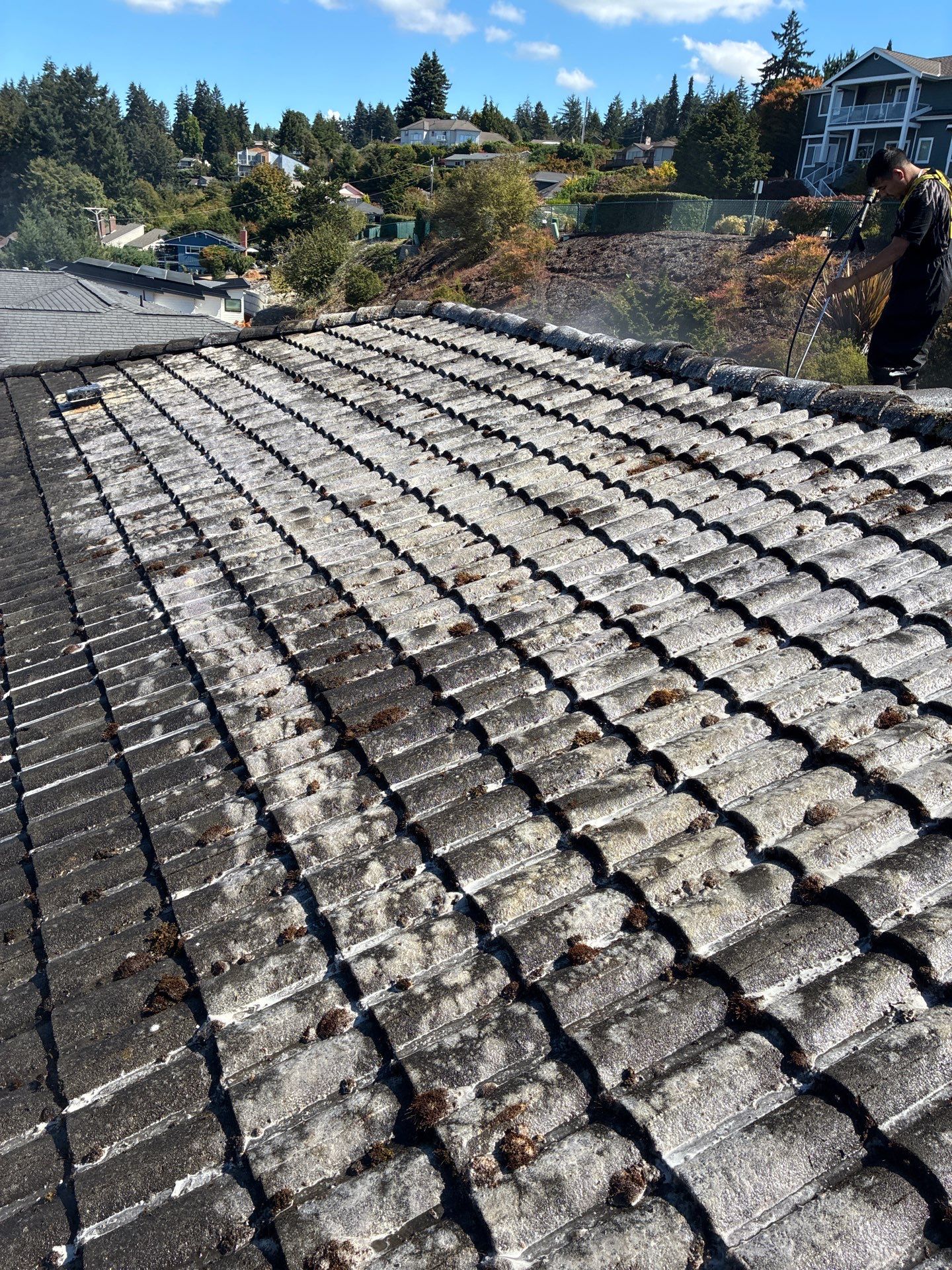 Homeworks Restoration technician washing concrete tile roof with specialized pressure equipment