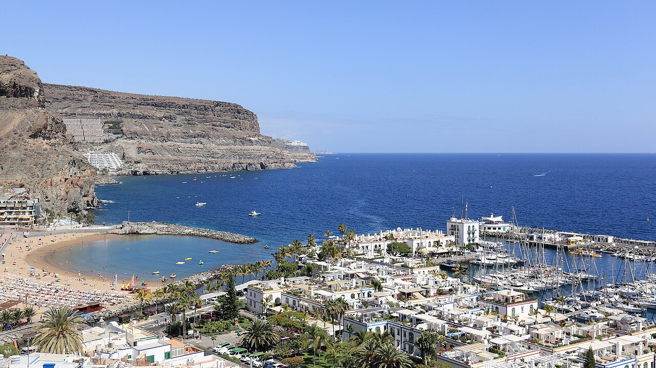 Vista panorámica de Puerto de Mogán mostrando el puerto deportivo, la playa semicircular, las embarcaciones y los acantilados