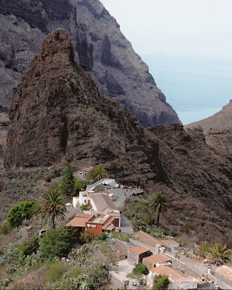 El caserío de Masca con sus casas tradicionales encaramadas sobre una cresta rocosa y palmeras canarias en el macizo de Teno