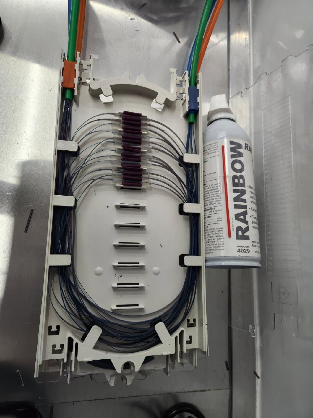Prepared fiber splice tray on stainless workstation with heat-shrink protection sleeves and cleaning spray