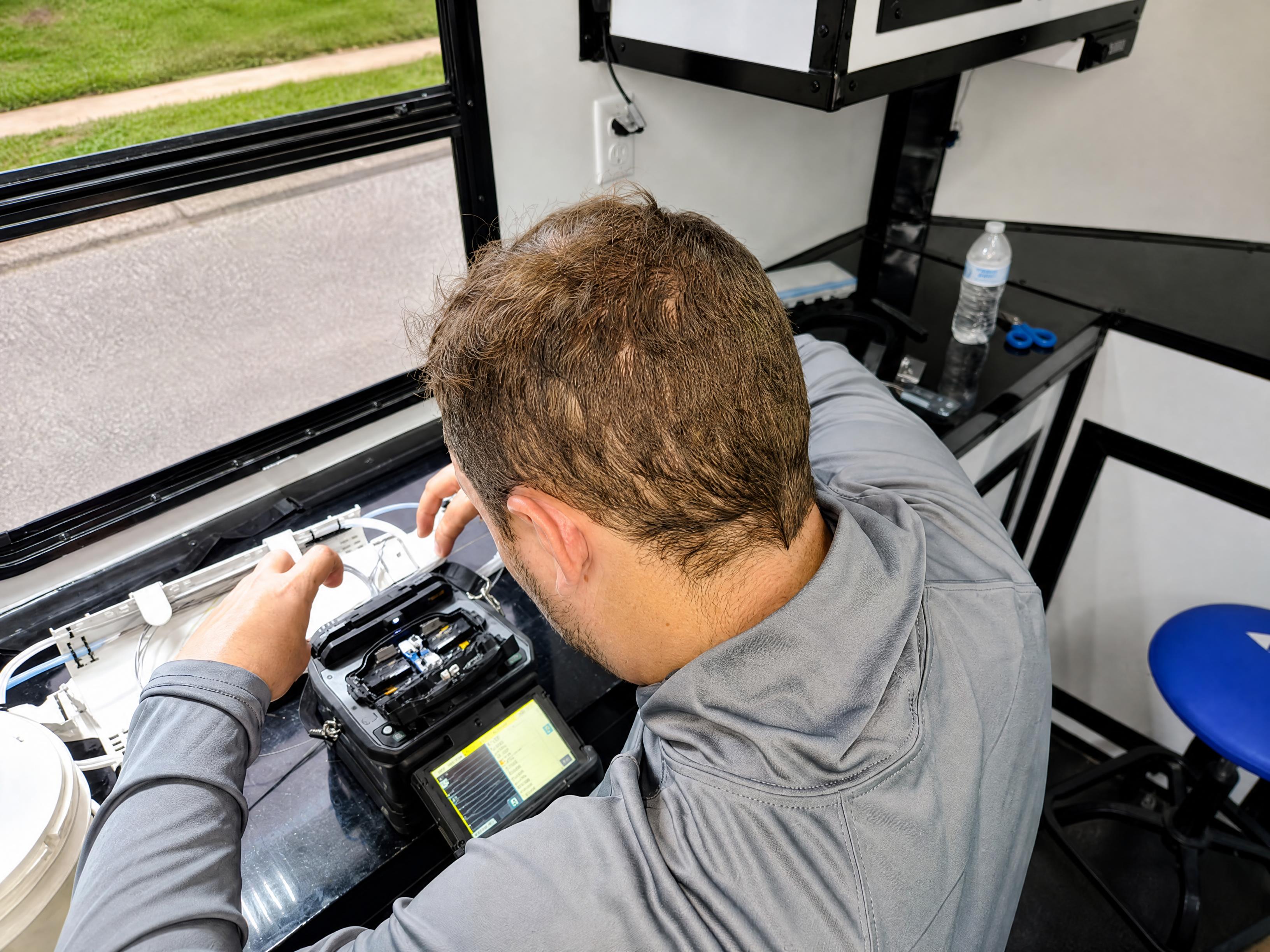 FAFO technician operating fusion splicer unit with active display in field environment