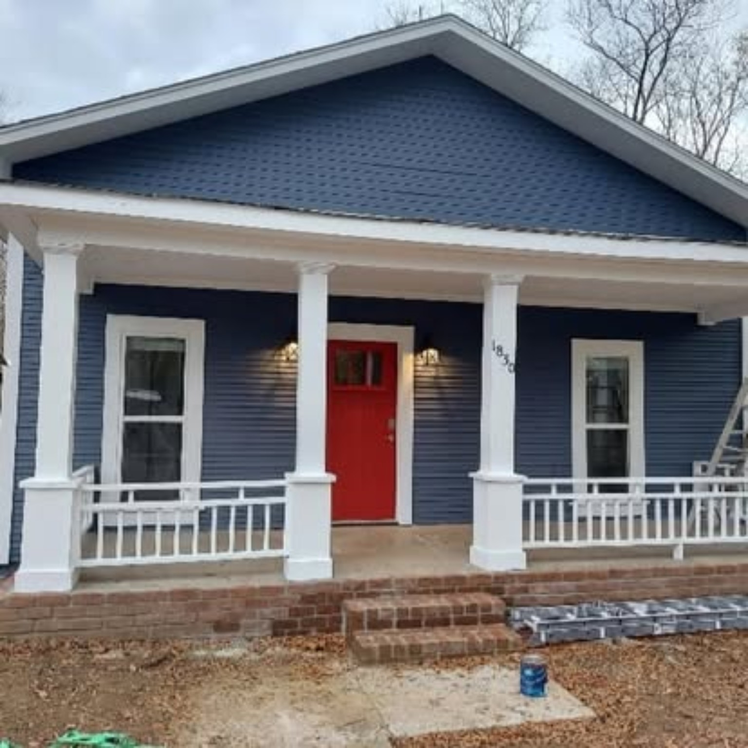 Completed deep navy blue house exterior with crisp white porch columns and bold red front door