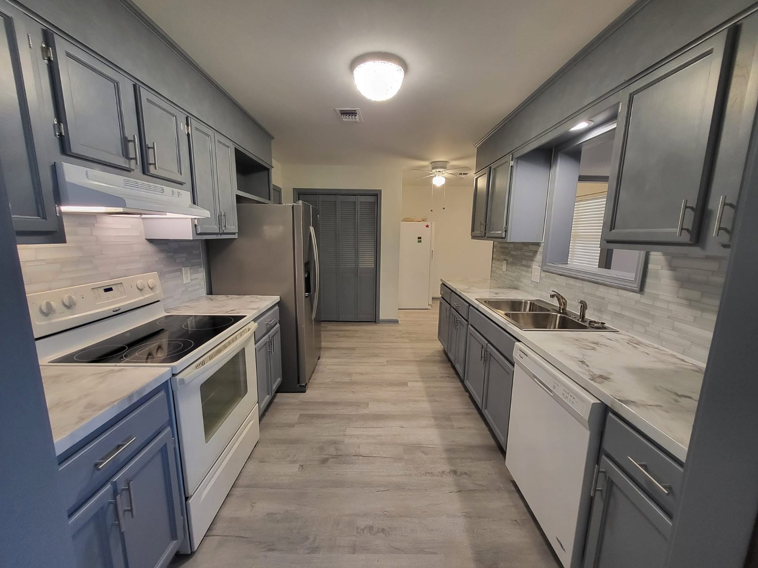 Galley kitchen completed view with freshly painted gray cabinets, marble countertops, and new flooring