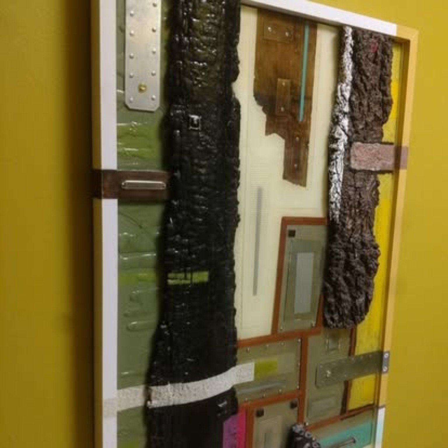 Dimensional mixed-media assemblage artwork angled side perspective highlighting 3D textures, charred wood, and metal plates