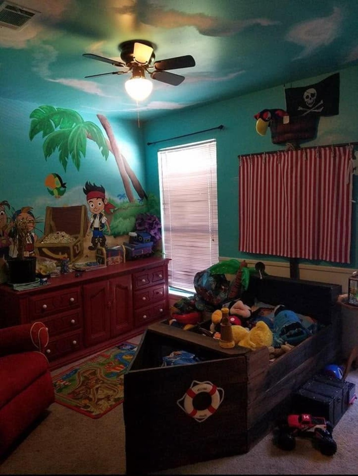 Pirate themed room with painted island mural, treasure chest, and custom wooden pirate ship bed