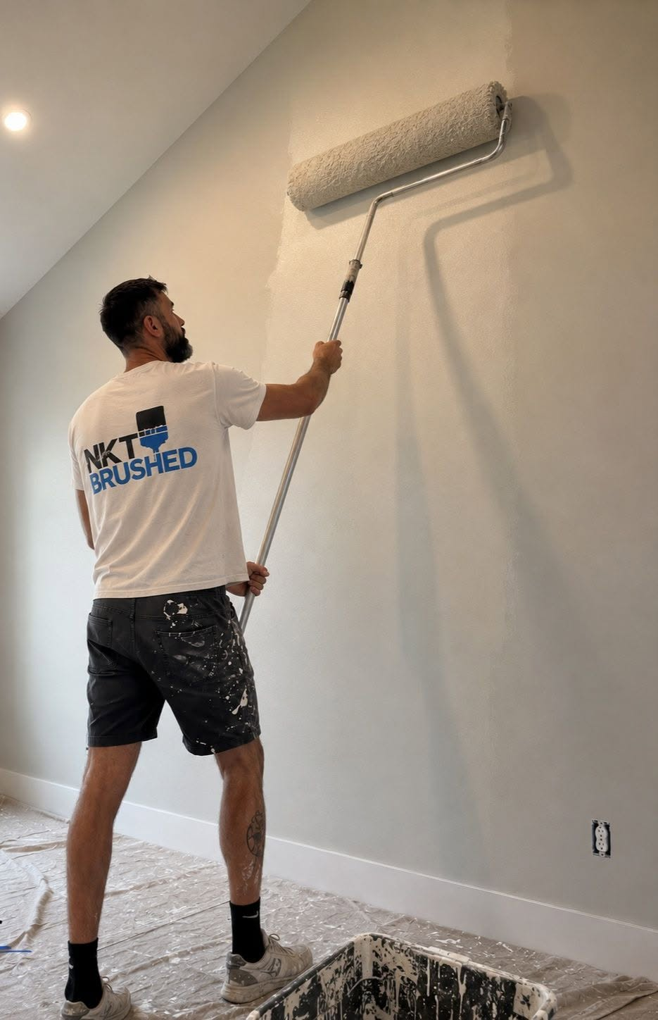 Nathan Terry painting a tall interior wall with roller extension and NKT Brushed shirt