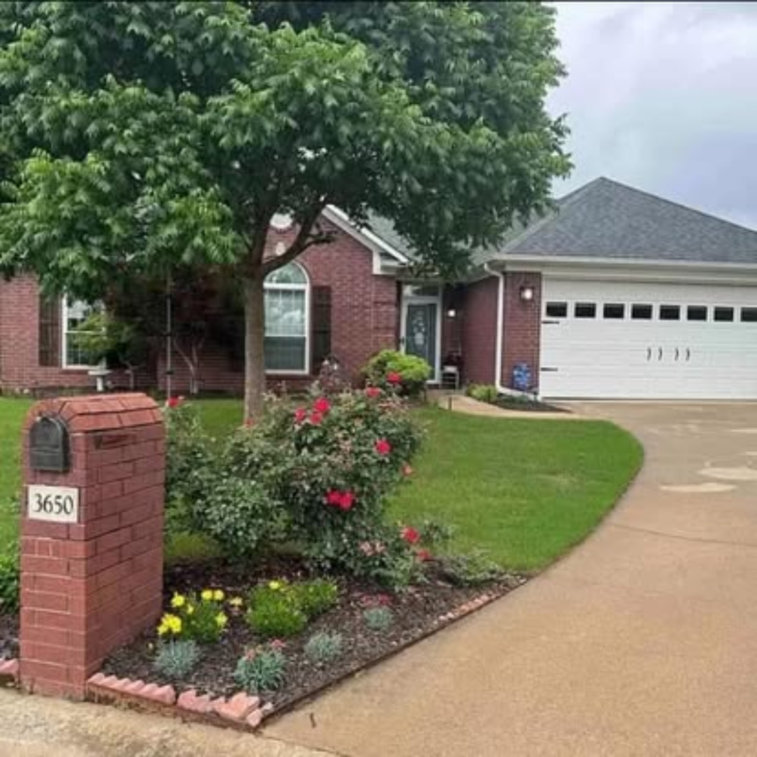 Red brick home before painting with dark roof and white garage door