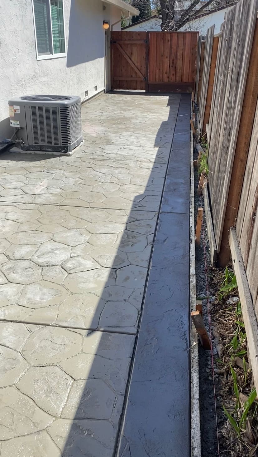 Side-yard decorative stamped concrete patio with contrasting border along fence line