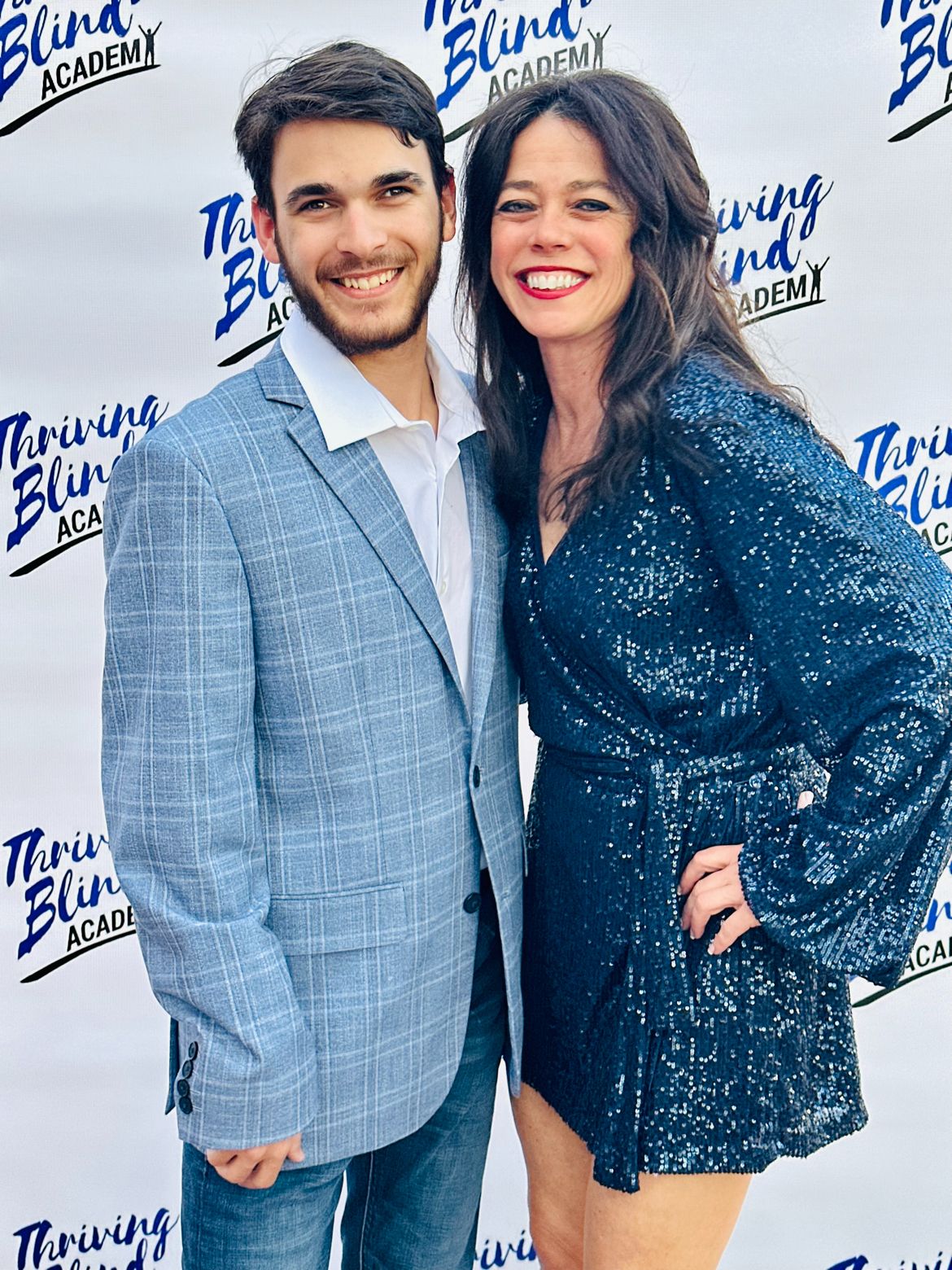 Author Kristin Smedley smiling beside her son Mitchell Smedley in front of a Thriving Blind Academy backdrop.