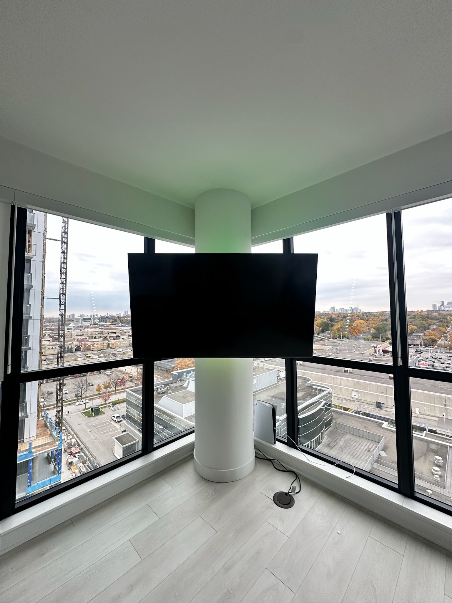 Television mounted to a round structural concrete pillar between corner condo windows in Toronto