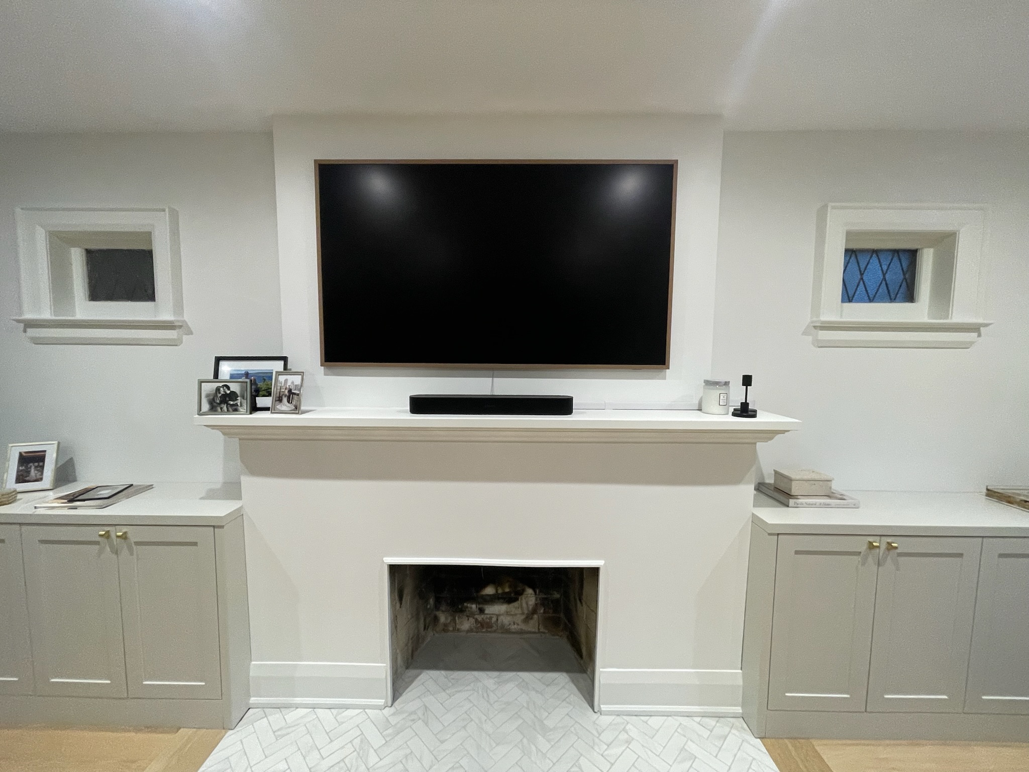 Mount Masters Samsung Frame TV with wood bezel flush mounted above white fireplace mantel and custom built-in cabinetry