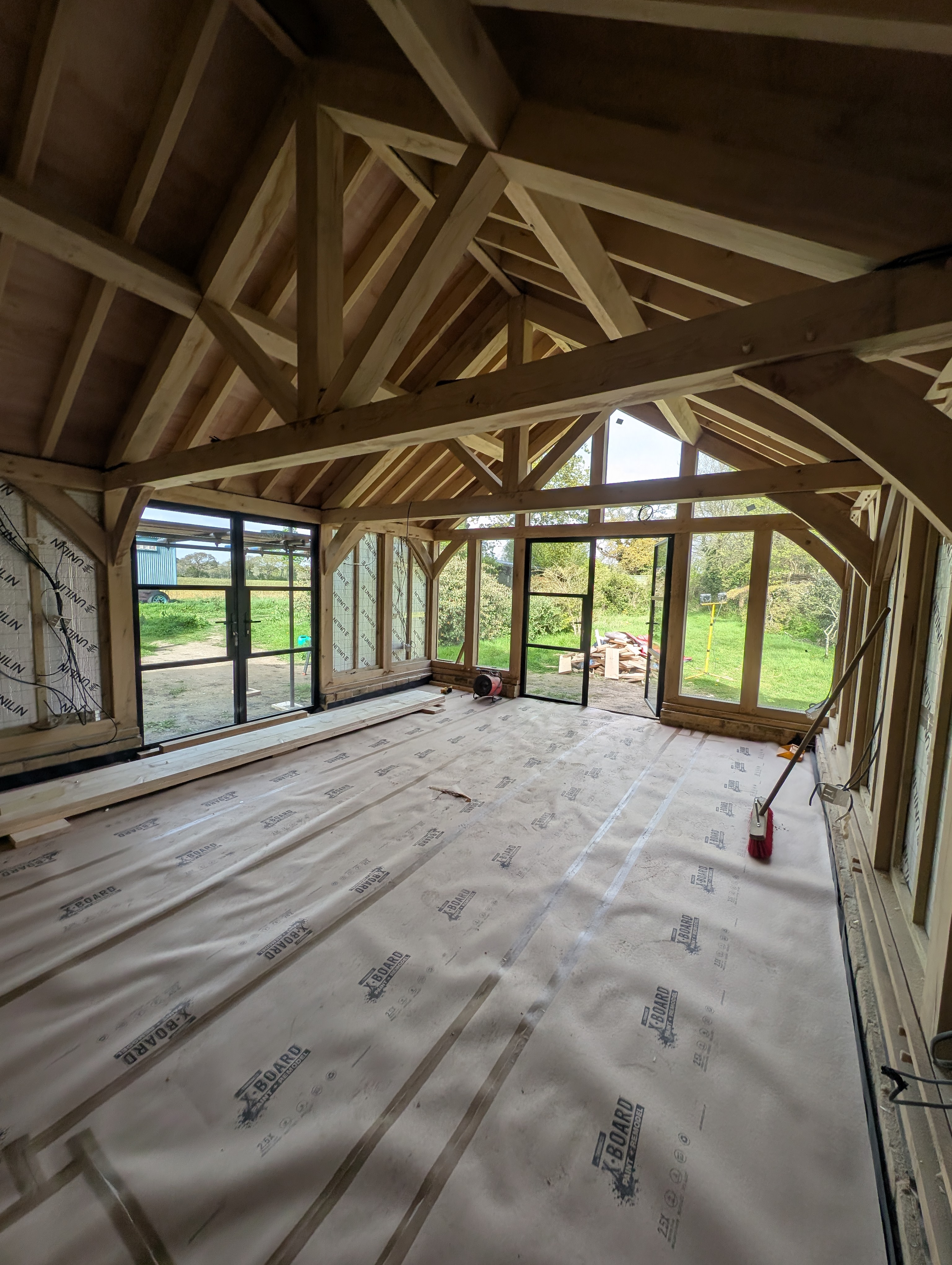 Green oak frame extension under construction showing vaulted timber trusses, glazed openings and floor protection