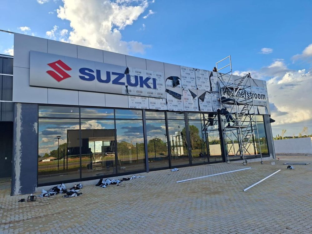 Suzuki dealership facade under construction with crew on scaffolding