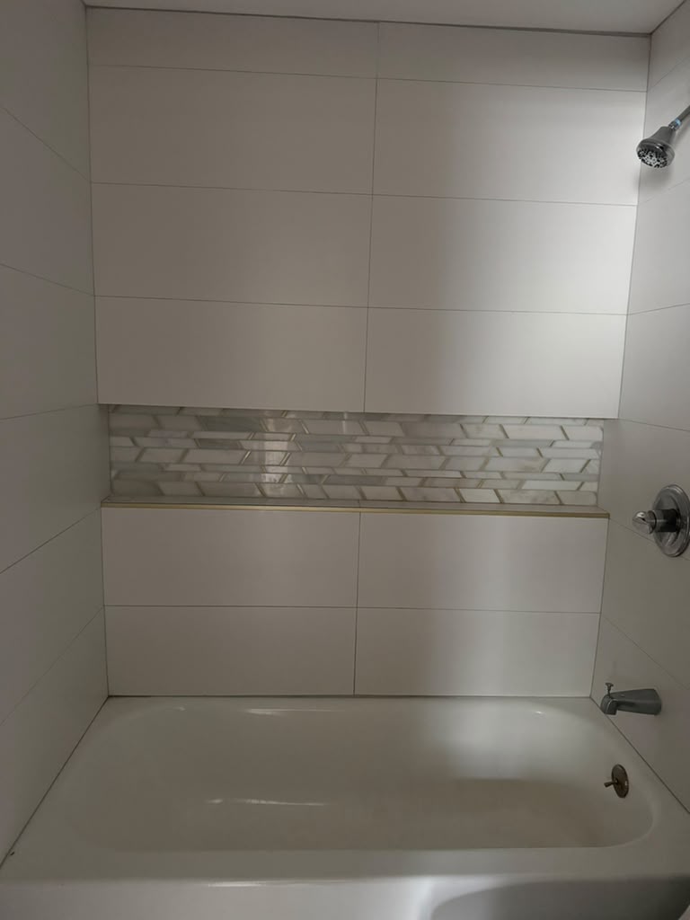 Modern white porcelain bathtub wall tile installation with horizontal mosaic accent shelf by LQJ General Construction in Smithtown NY