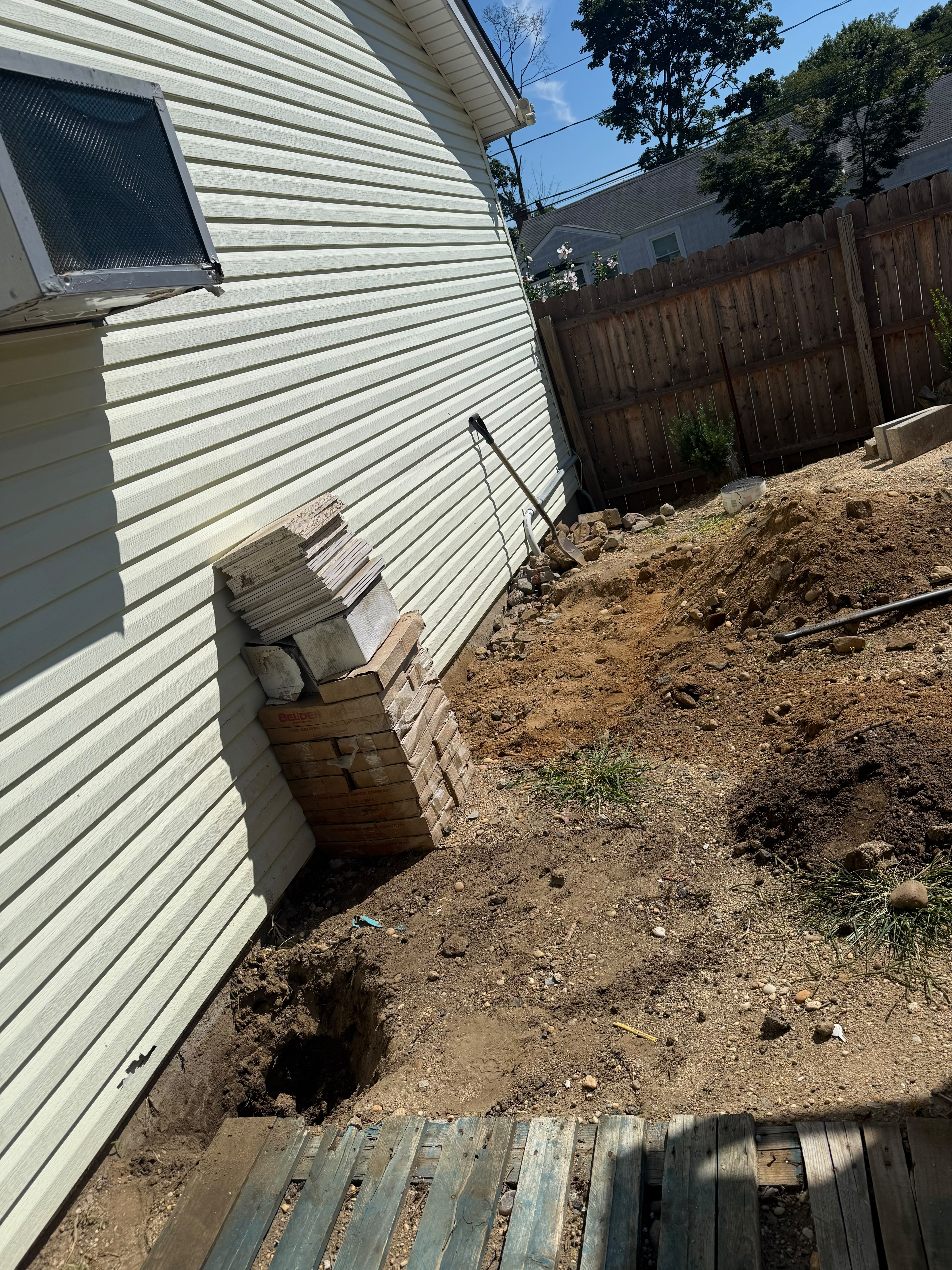 Excavation trenching, deep structural footing hole, and stacked Belden brick pavers along residential siding by LQJ General Construction in Central Islip NY