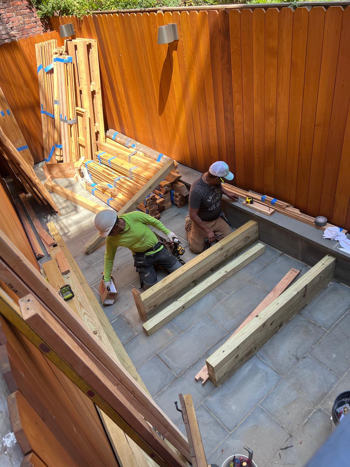 LQJ General Construction carpenters assembling floor support joists inside cedar fenced courtyard