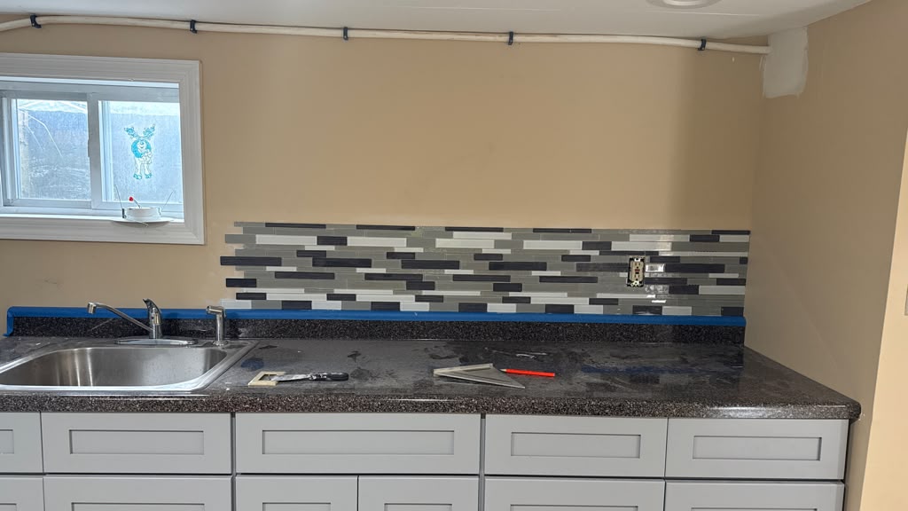 Detailed view of linear glass mosaic tile backsplash installation with blue tape prep by LQJ General Construction in Hauppauge NY