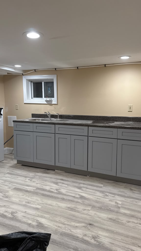 Full view of grey shaker kitchenette base cabinets and waterproof wood-look vinyl plank flooring by LQJ General Construction in Hauppauge NY
