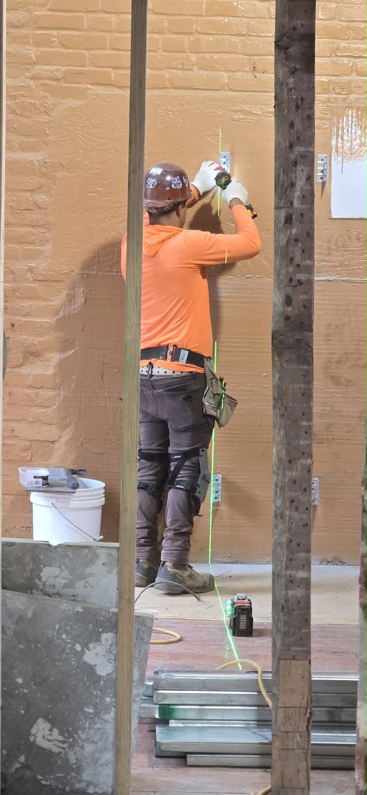 Craftsman using green laser level for structural wall bracket alignment by LQJ General Construction in Central Islip NY