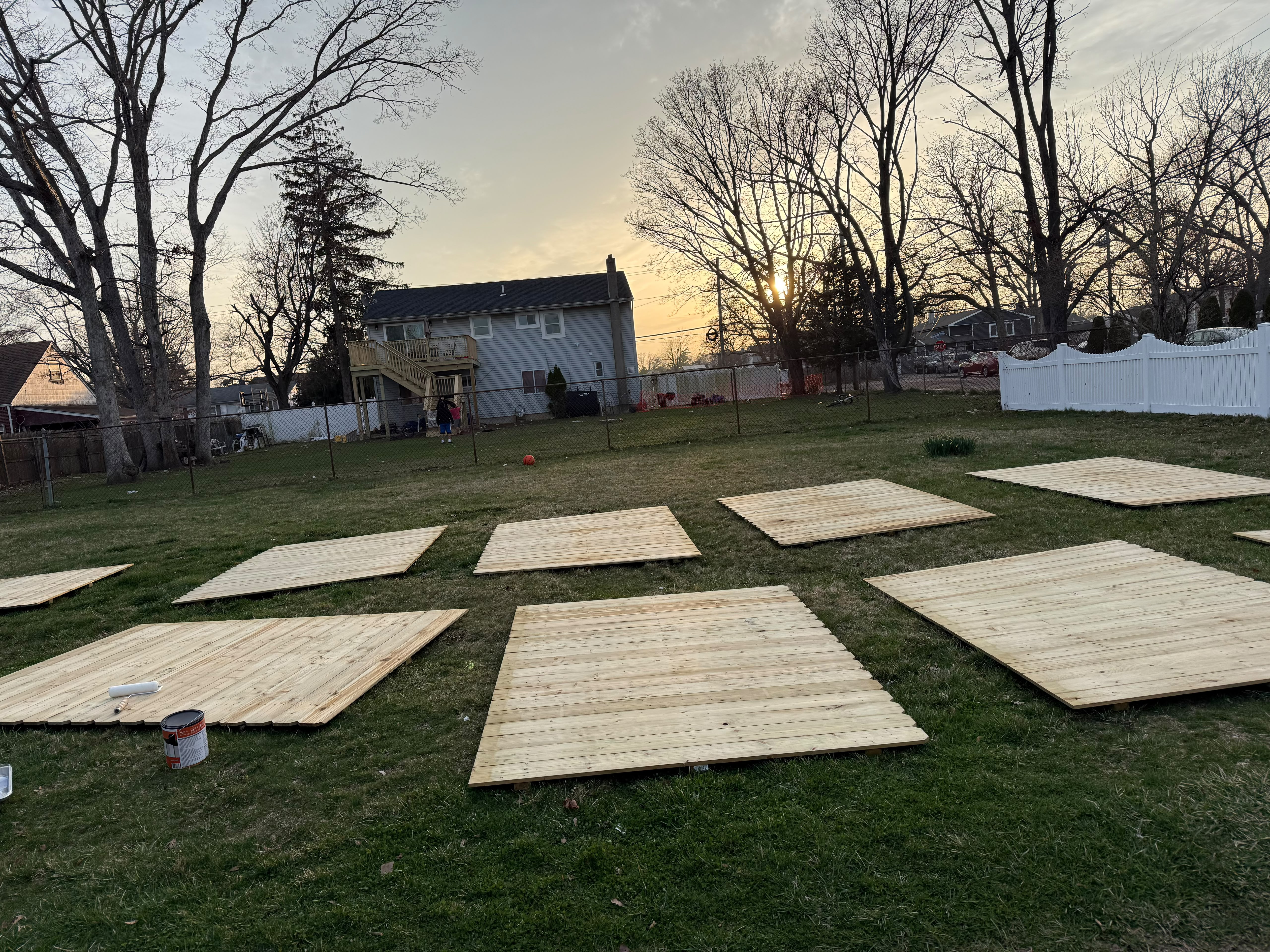 Custom pressure-treated wood privacy fence panels laid out on residential lawn for staging and protective sealing by LQJ General Construction in Commack NY