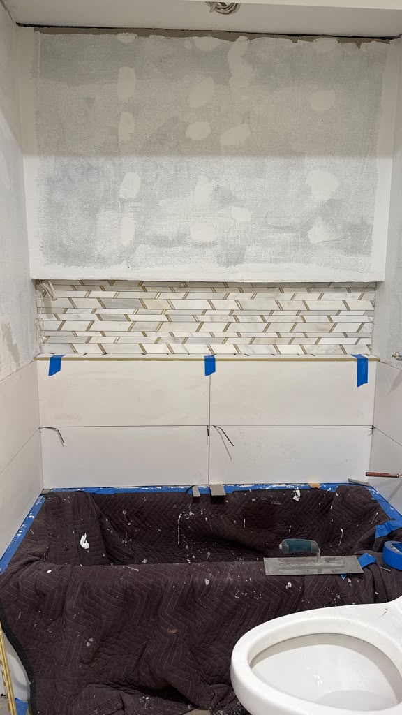 In-progress large-format bathroom tile installation with herringbone mosaic shampoo niche and brass edge trim by LQJ General Construction in Smithtown NY