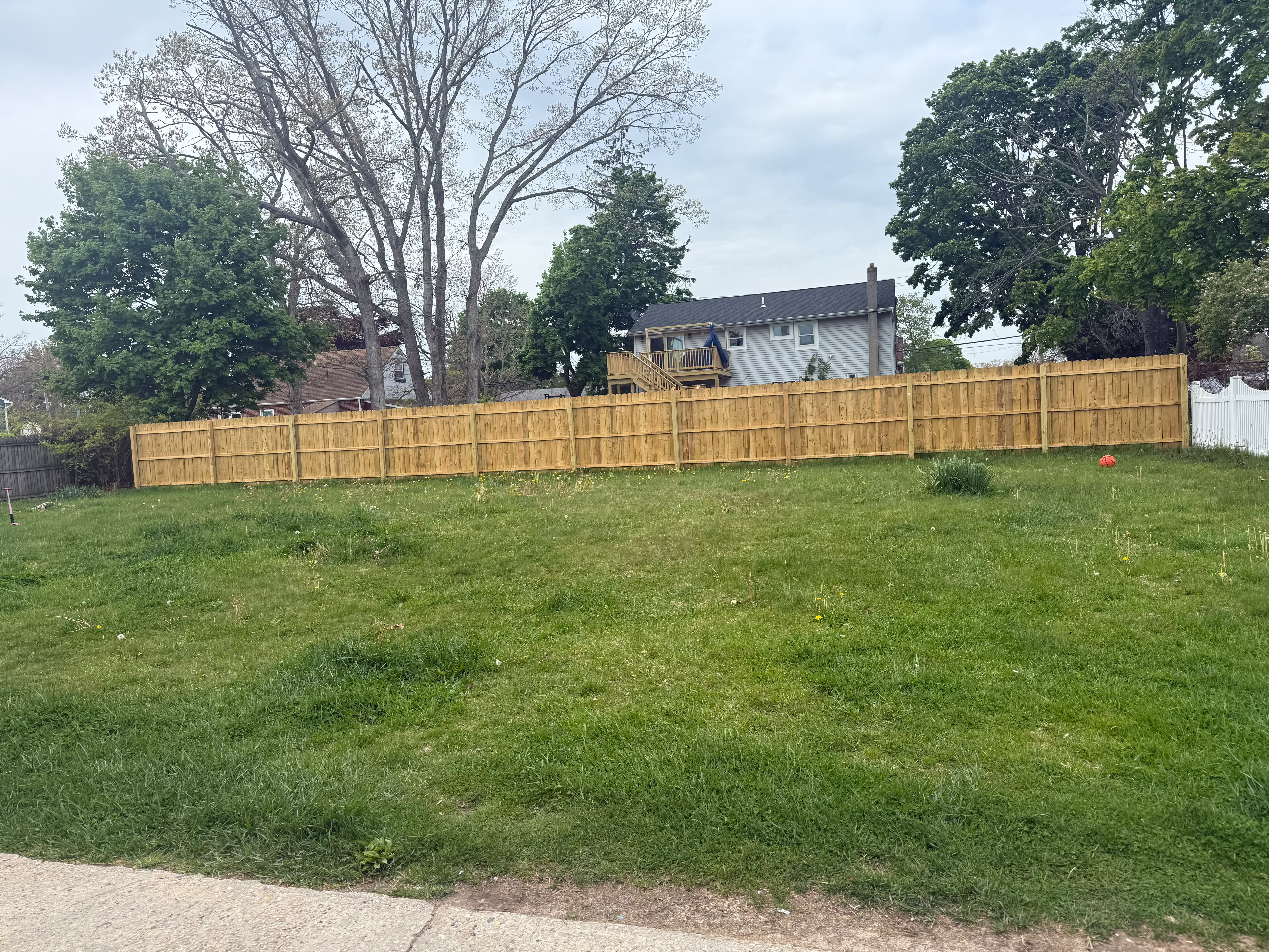 Finished 6-foot wood privacy fence line bordering spacious green suburban backyard by LQJ General Construction in Commack NY