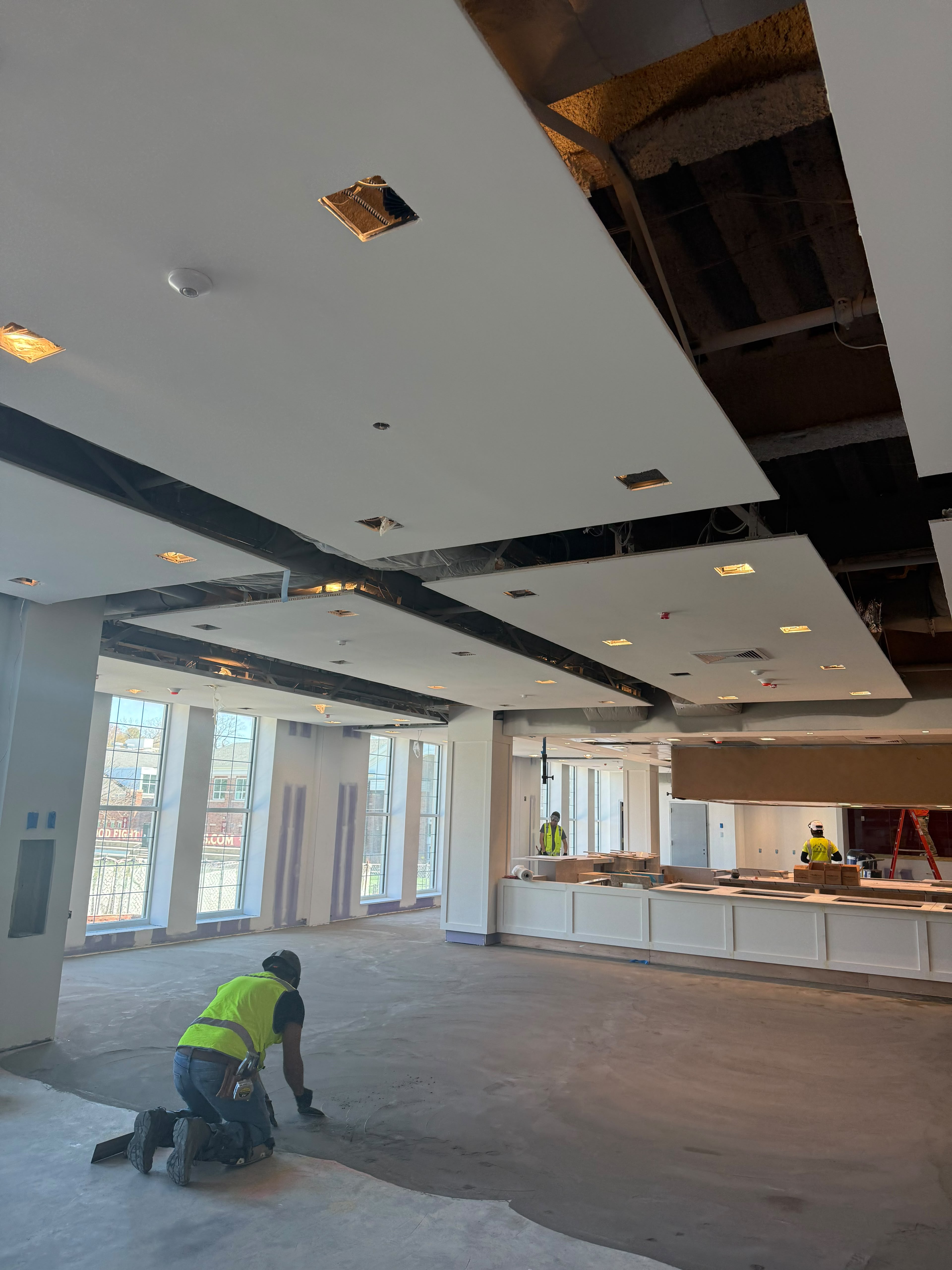 Craftsman hand-troweling concrete subfloor under architectural floating ceiling clouds by LQJ General Construction in Hauppauge NY