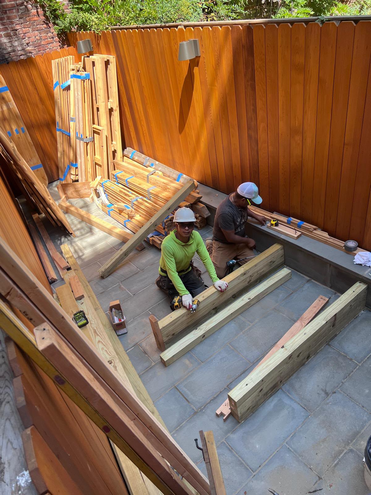 LQJ General Construction carpenters assembling pressure-treated deck joists inside cedar privacy fenced courtyard in Northport NY