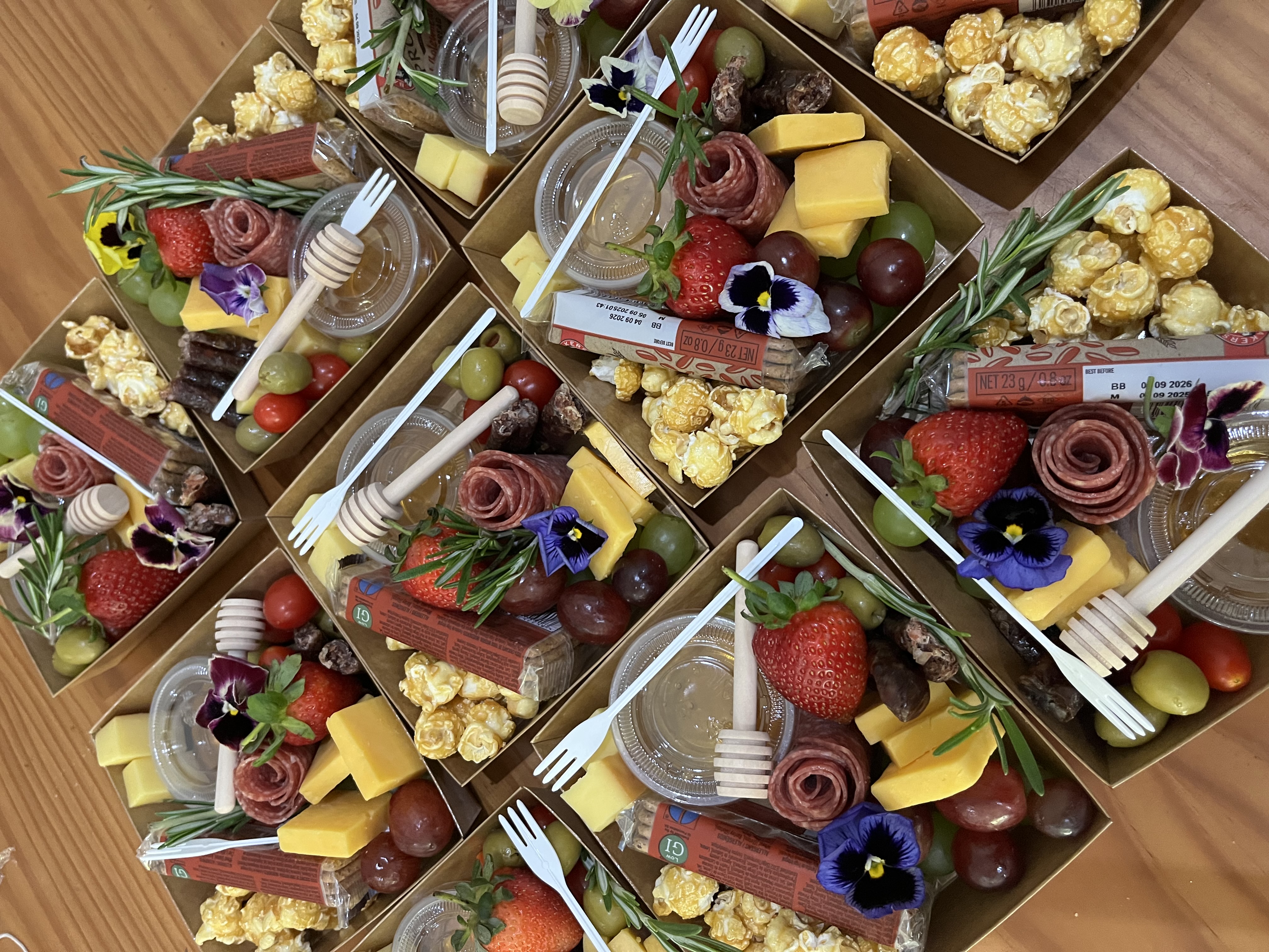 Artisan charcuterie boxes prepared with salami rose, cheeses, strawberries, honey dippers and edible flowers