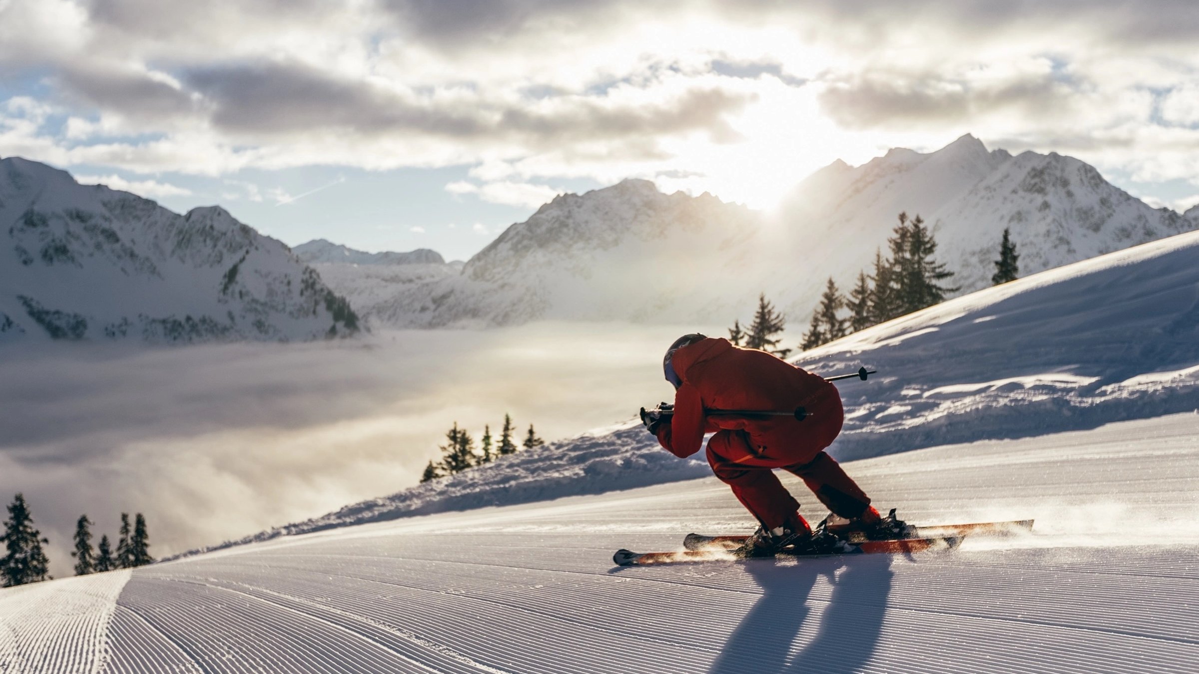 Skifahrer im roten Rennanzug bei Sonnenuntergang über den Wolken, Oliver Farys