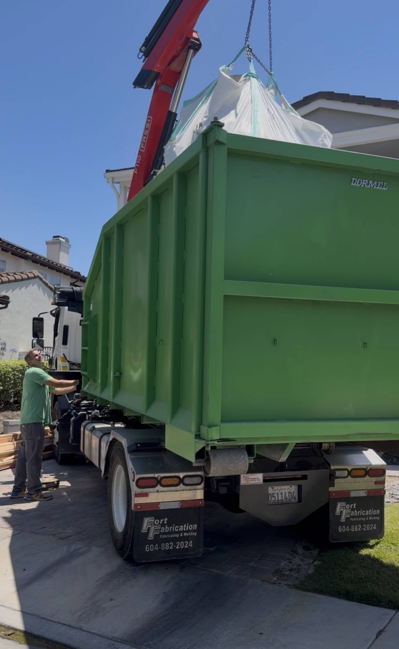 Crane lowering a full dumpster bag directly into the Eco Waste roll-off truck