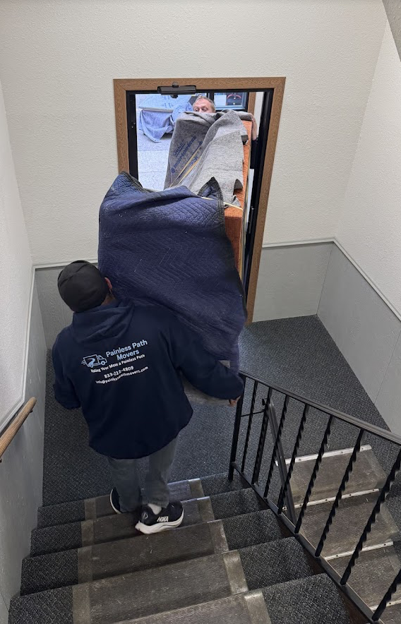 Painless Path Movers crew in official company hoodie carrying padded furniture downstairs