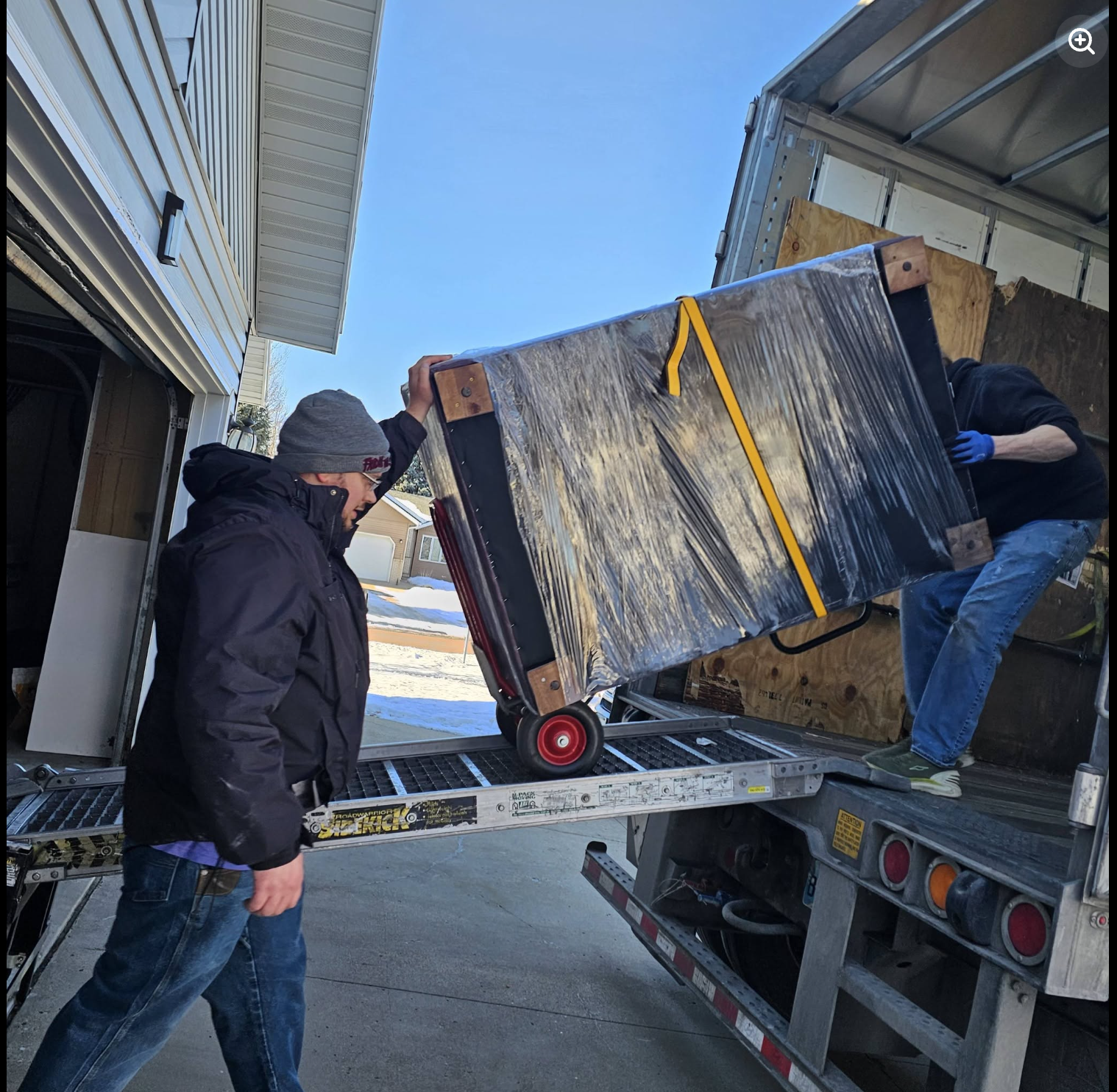 Painless Path Movers crew wheeling shrink-wrapped furniture up the loading ramp into moving truck