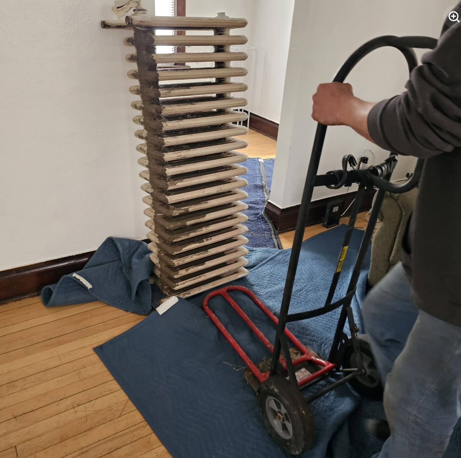 Painless Path Movers crew using padded moving blankets and heavy-duty hand truck dolly to remove heavy cast-iron radiator from home