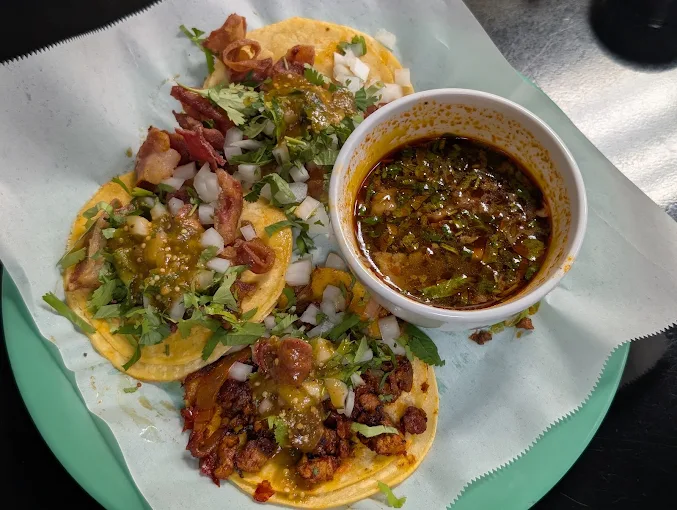 Street tacos garnished with cilantro, onions, and salsa served with rich savory consomé dipping broth