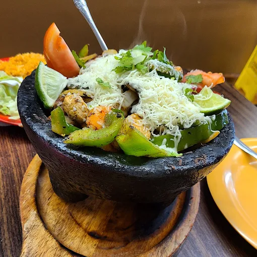 Steaming hot traditional volcanic stone molcajete loaded with grilled peppers, cheese, meats, and fresh limes