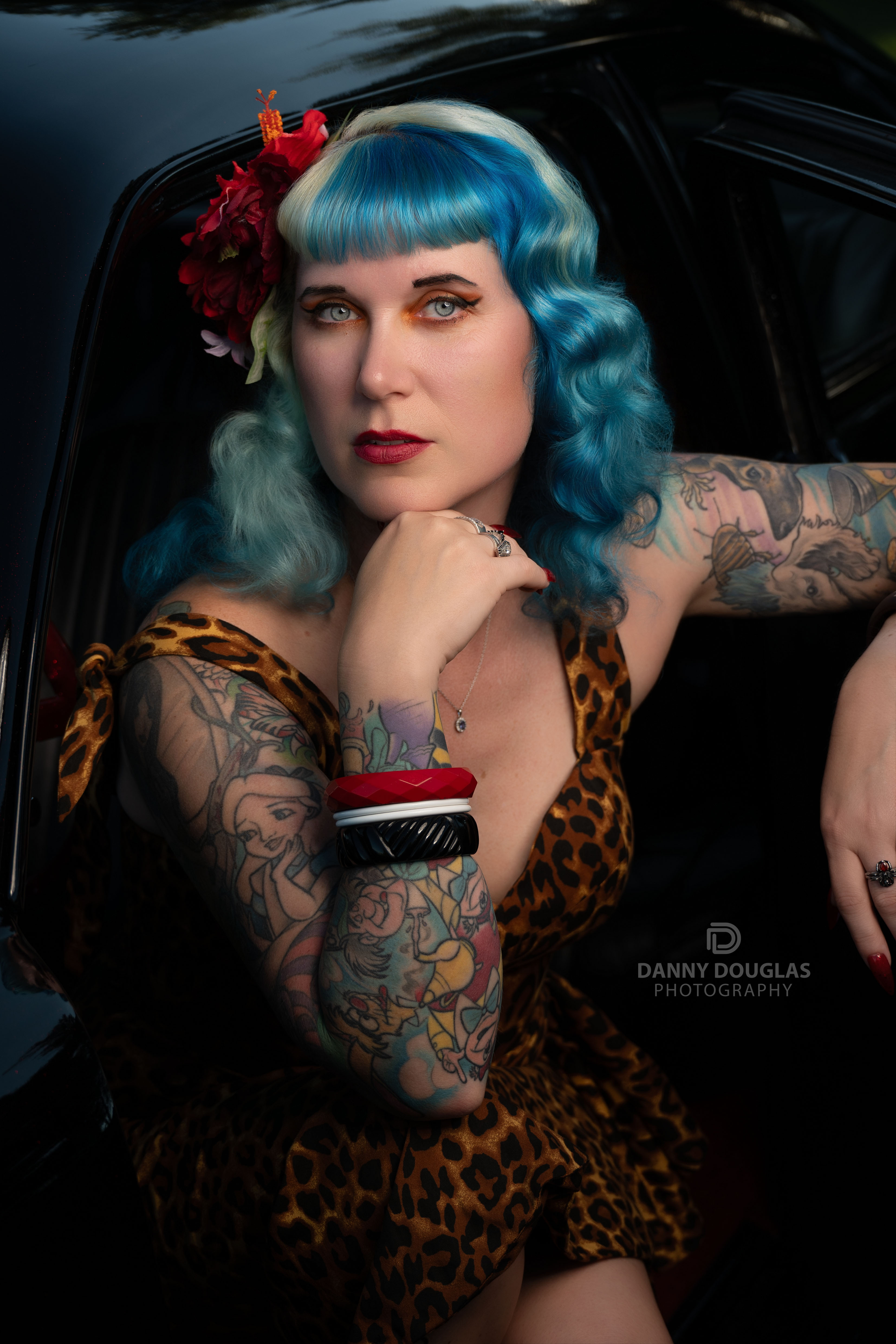 Danny Douglas Photography rockabilly pin-up model with blue hair, vintage leopard print dress, and tattoo sleeve in a classic car