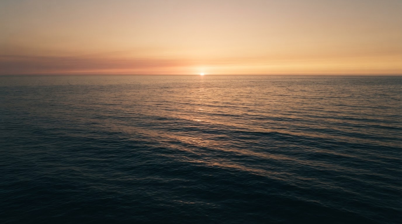 Calm ocean water meeting a soft golden horizon at dusk
