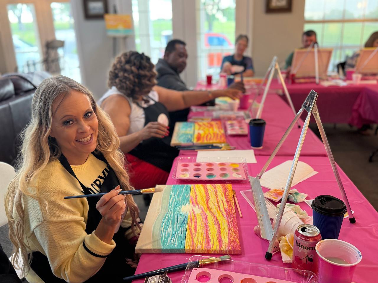Retreat guest smiling while painting a sunset canvas during an Encounter creative session