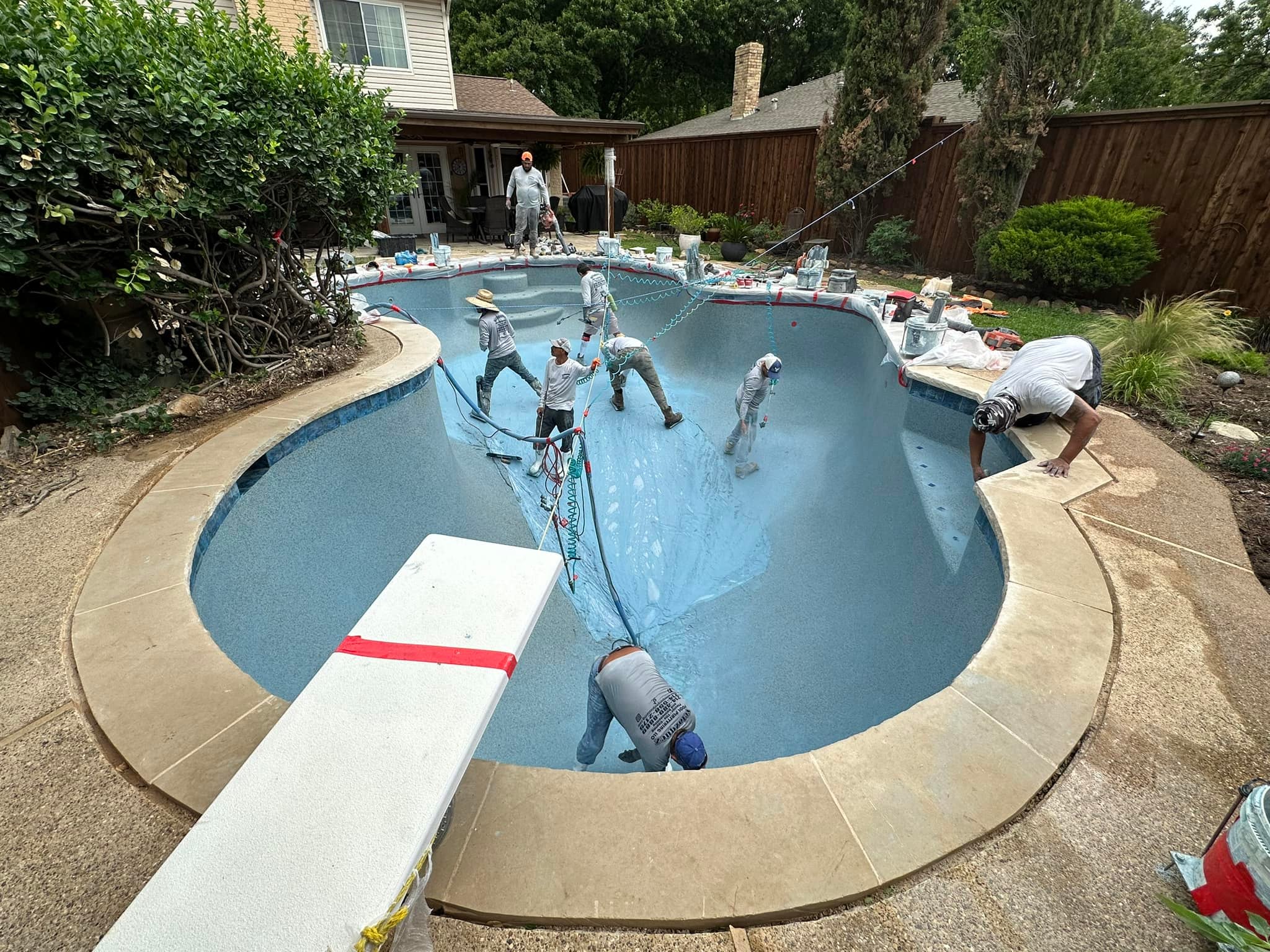 Pool-finishing crew applying a new interior surface inside a drained swimming pool
