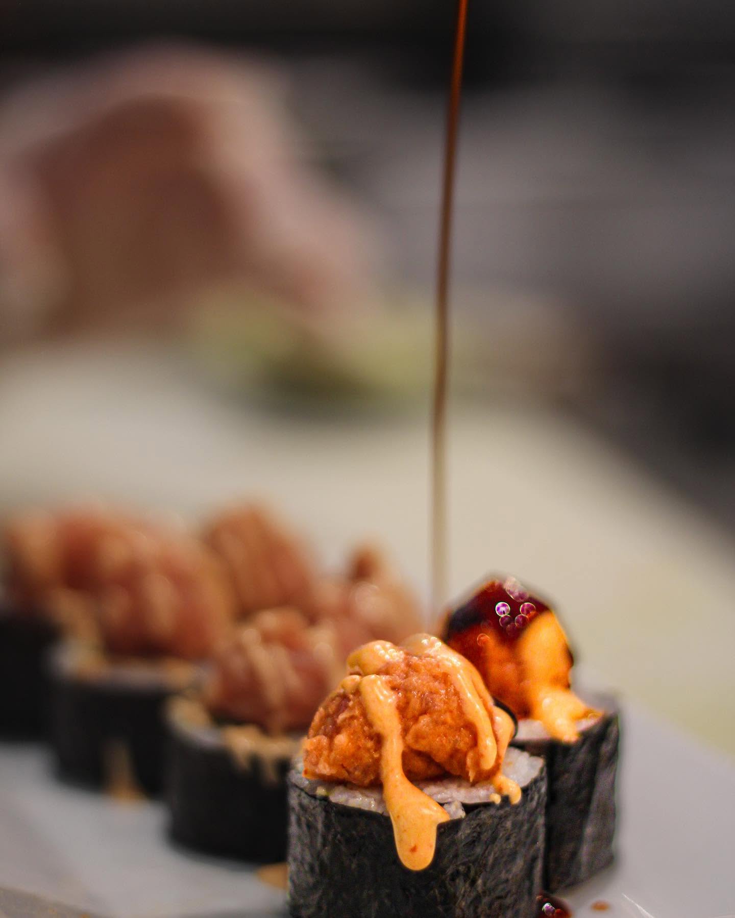 Artisan sushi roll getting drizzled with sweet savory eel sauce and spicy aioli at Nori in Omaha