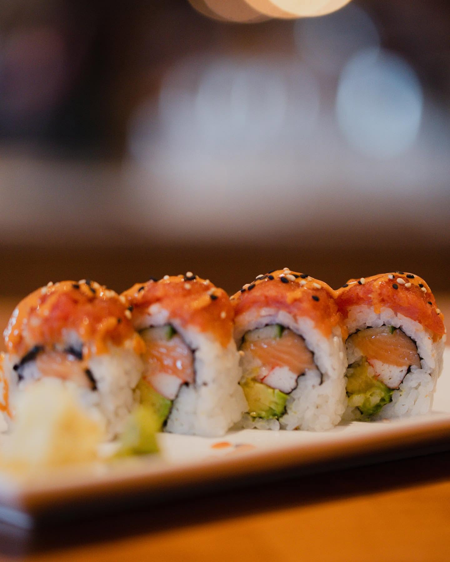 Four pieces of fresh spicy salmon avocado sushi roll topped with seasoned fish tartare and black sesame at Nori in Omaha