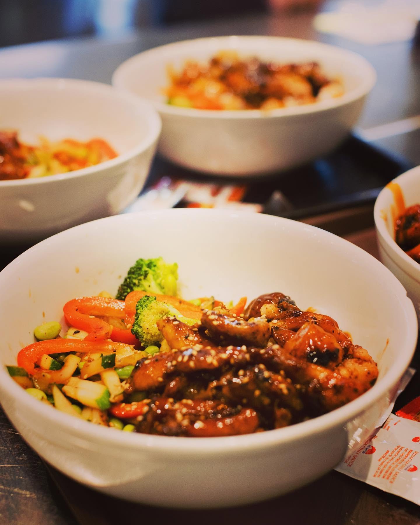 Savory glazed teriyaki chicken bowl with sesame seeds, broccoli, and peppers served in white bowls at Nori in Omaha