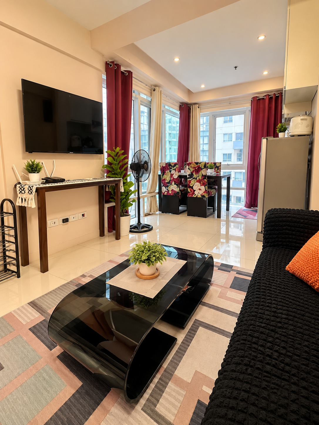 Real Lily Bloom living and dining shared common area with black sofa, modern glass coffee table, wall television, window, and dining setup