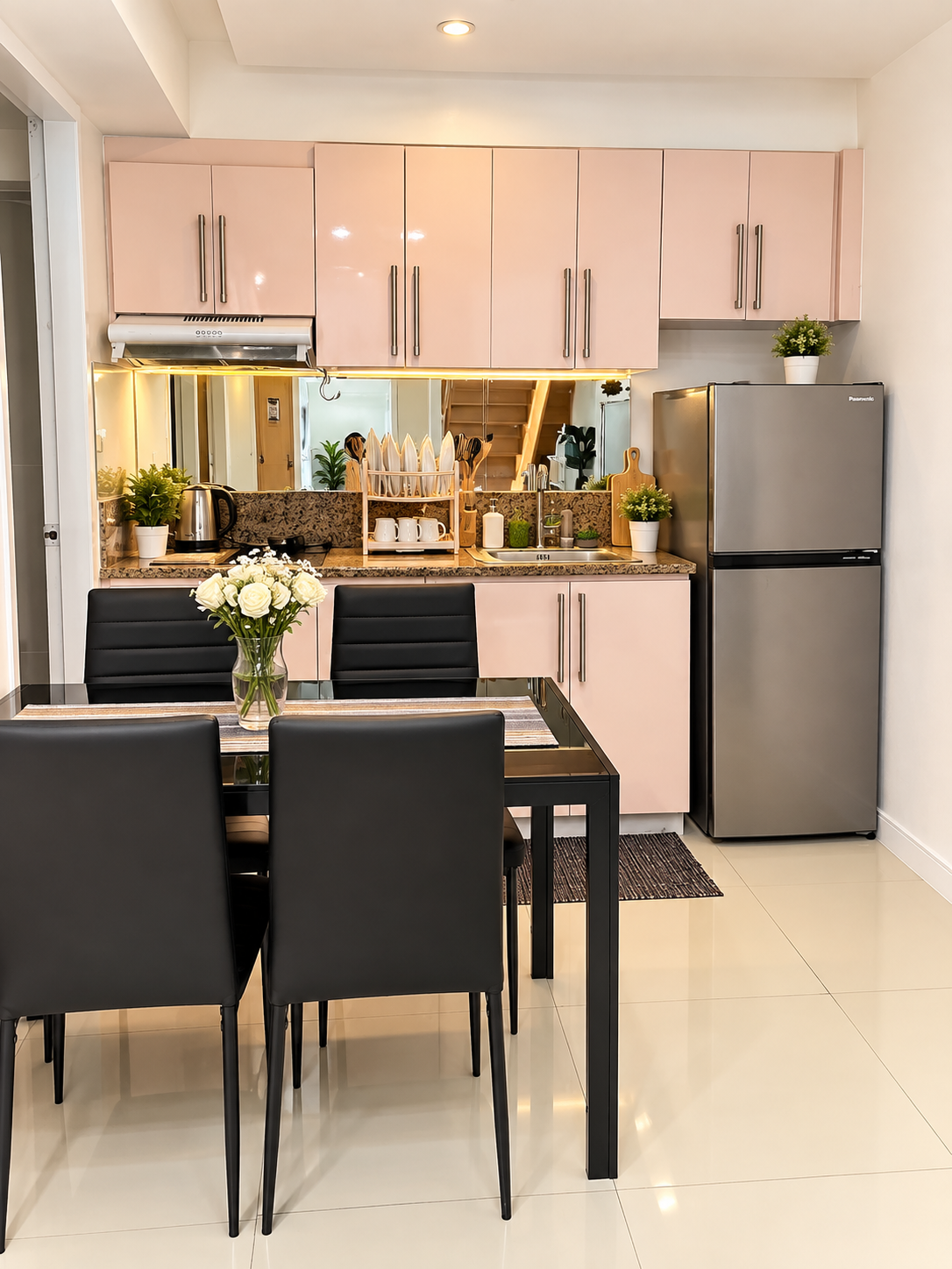 Real Lily Bloom shared kitchen and dining area featuring soft blush-pink cabinetry, dining table with floral centerpiece, and refrigerator