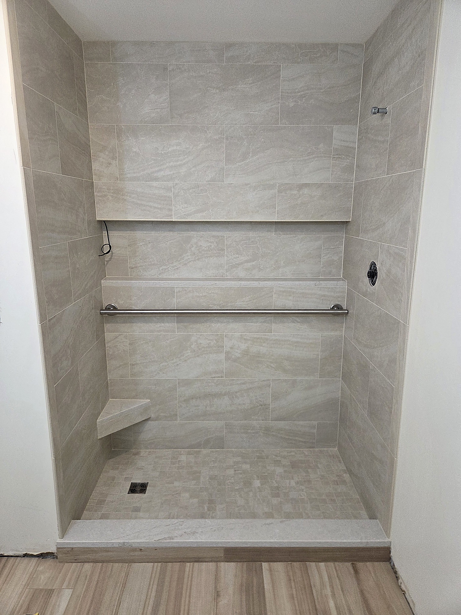 Tiled shower with stone-look wall tile, corner bench and mosaic floor